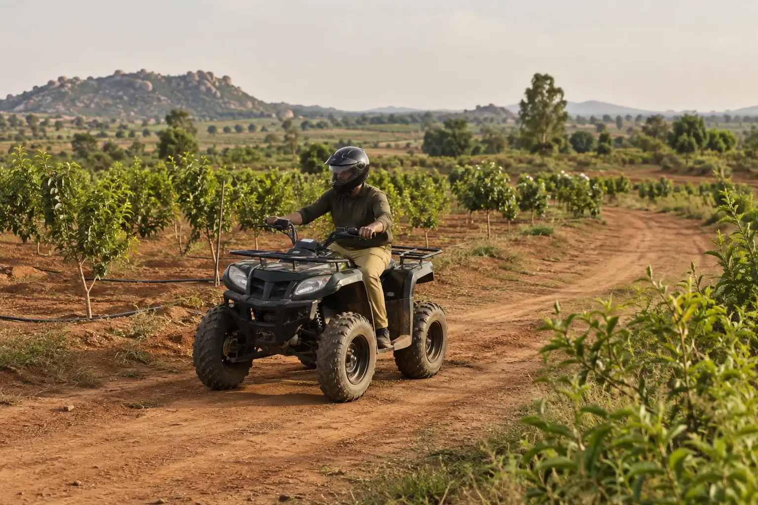 A rider in a helmet on a four-wheel ATV on an earthen farm track.